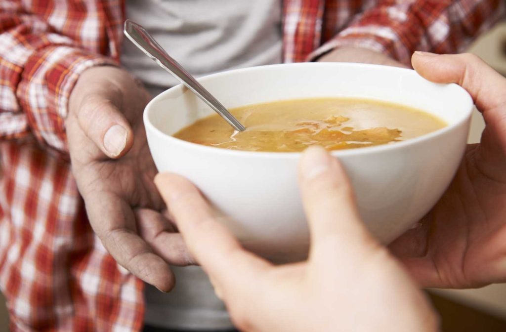man in checkered shirt receiving a bowl of soup from volunteer's hands gratefully
