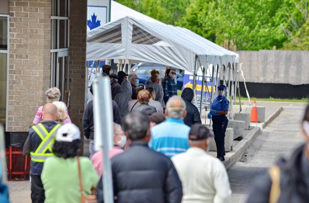 deep focus photo of Ontario lineups for covid-19 health assessments with white tent and brick building background