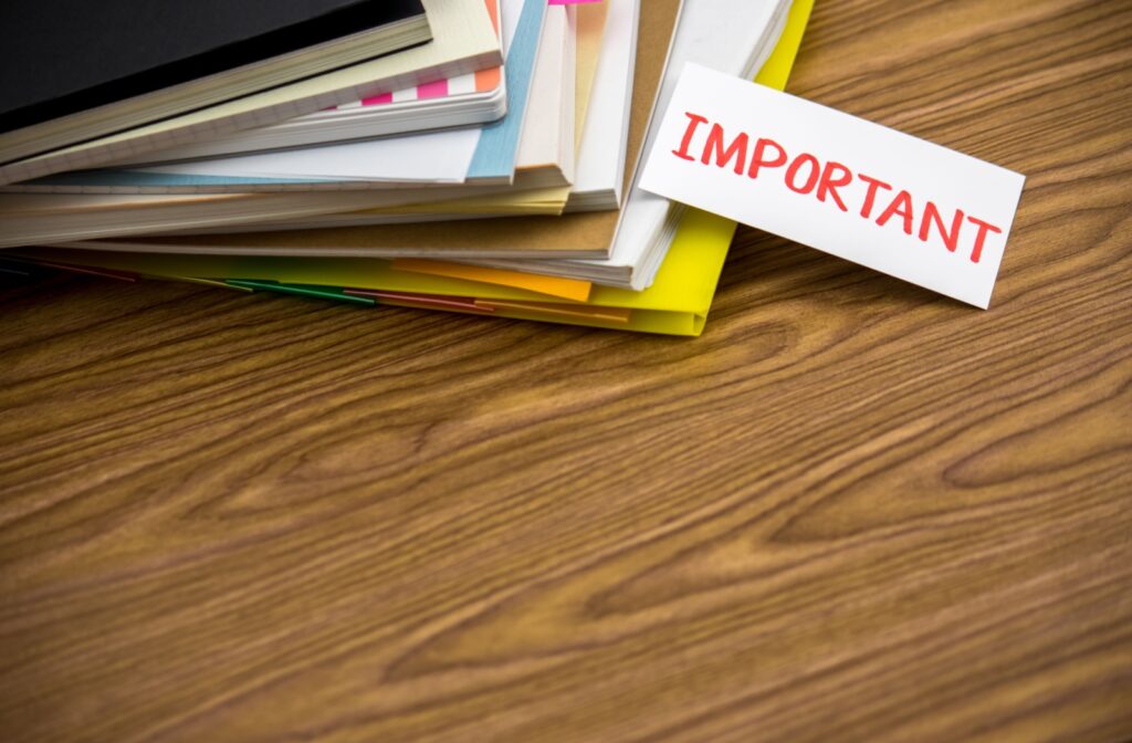 A pile of notebooks and paperwork layered on a desk with a note stating "important".
